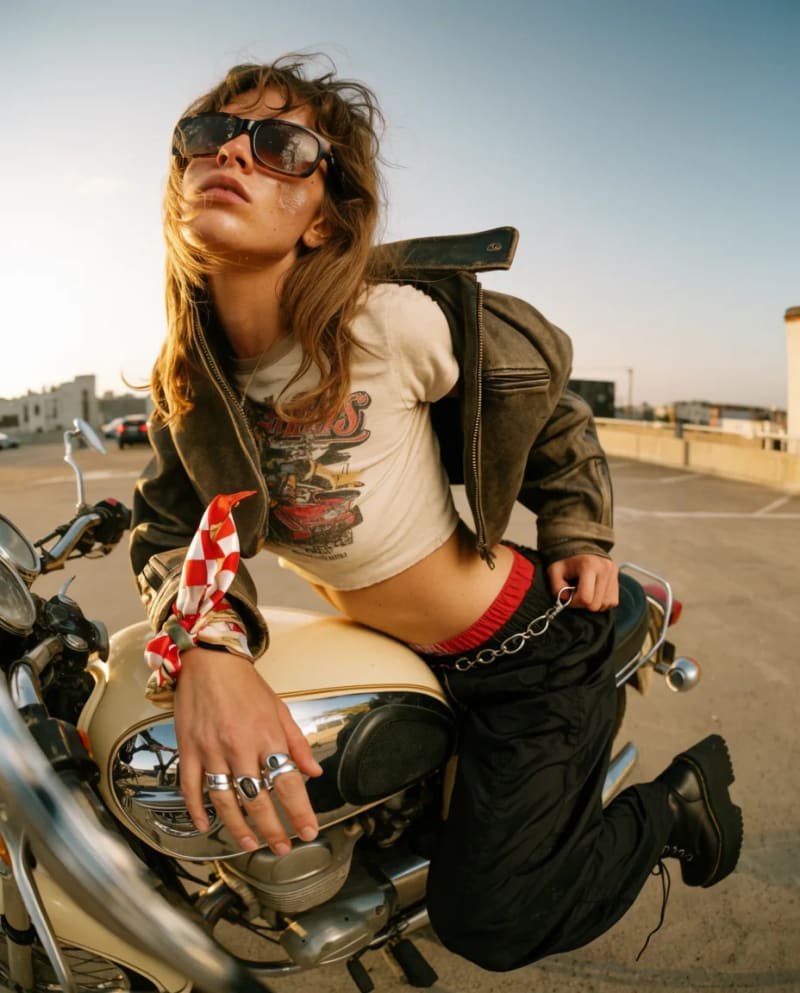 Model in sunglasses and a leather jacket leaning on a motorcycle on a rooftop