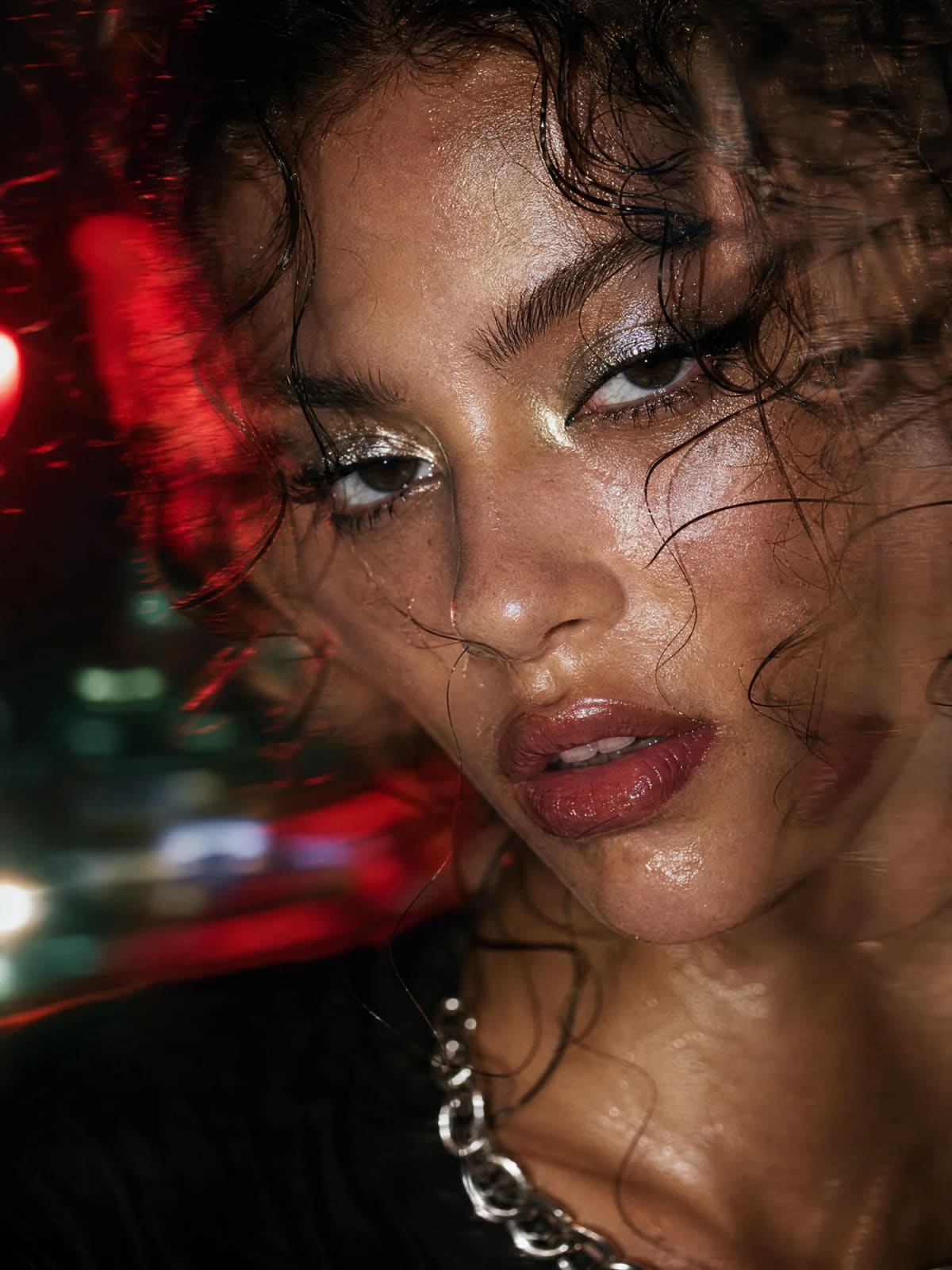 Close-up portrait with glossy skin and red city lights