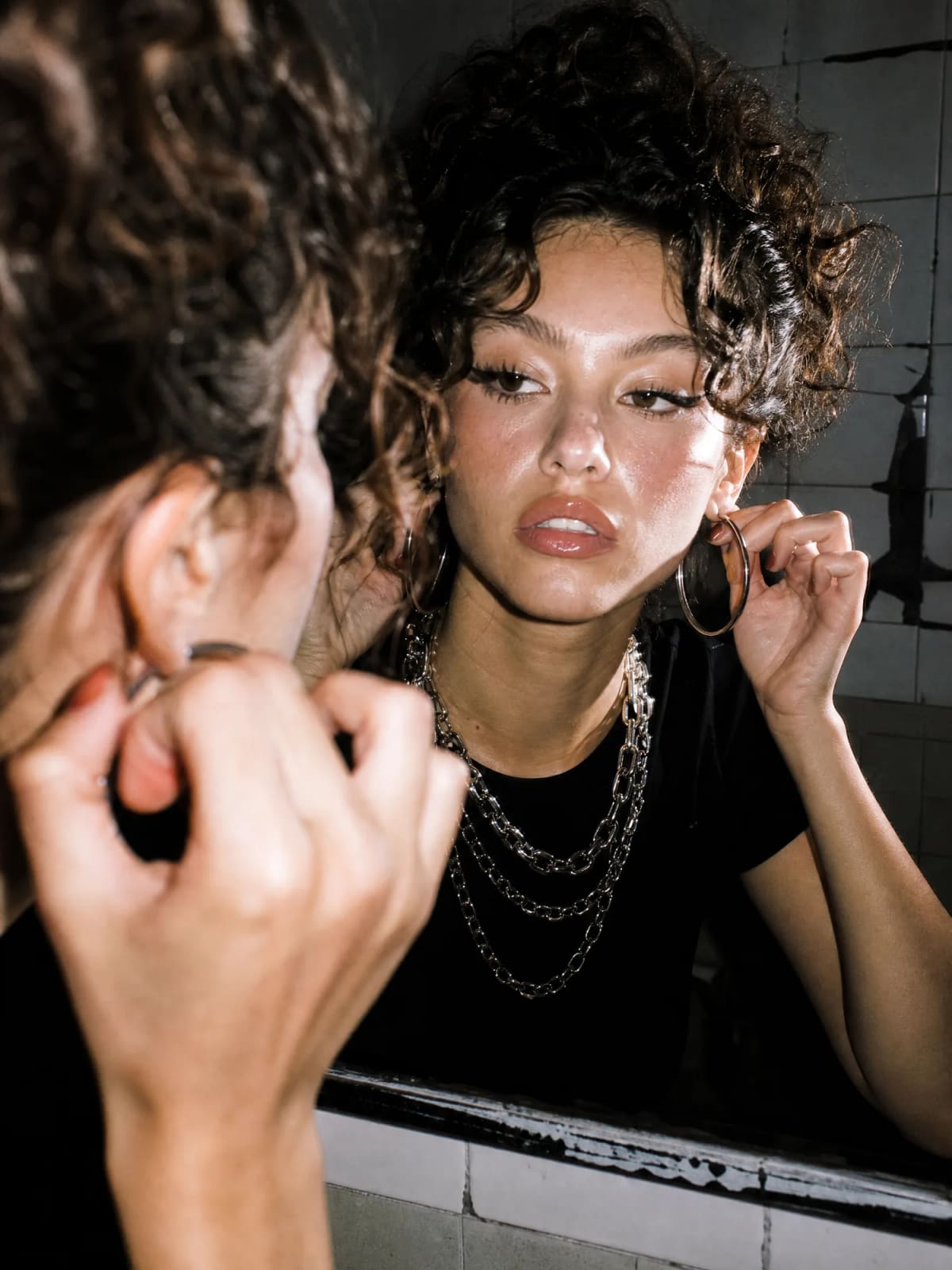 Model adjusting a hoop earring in a mirror